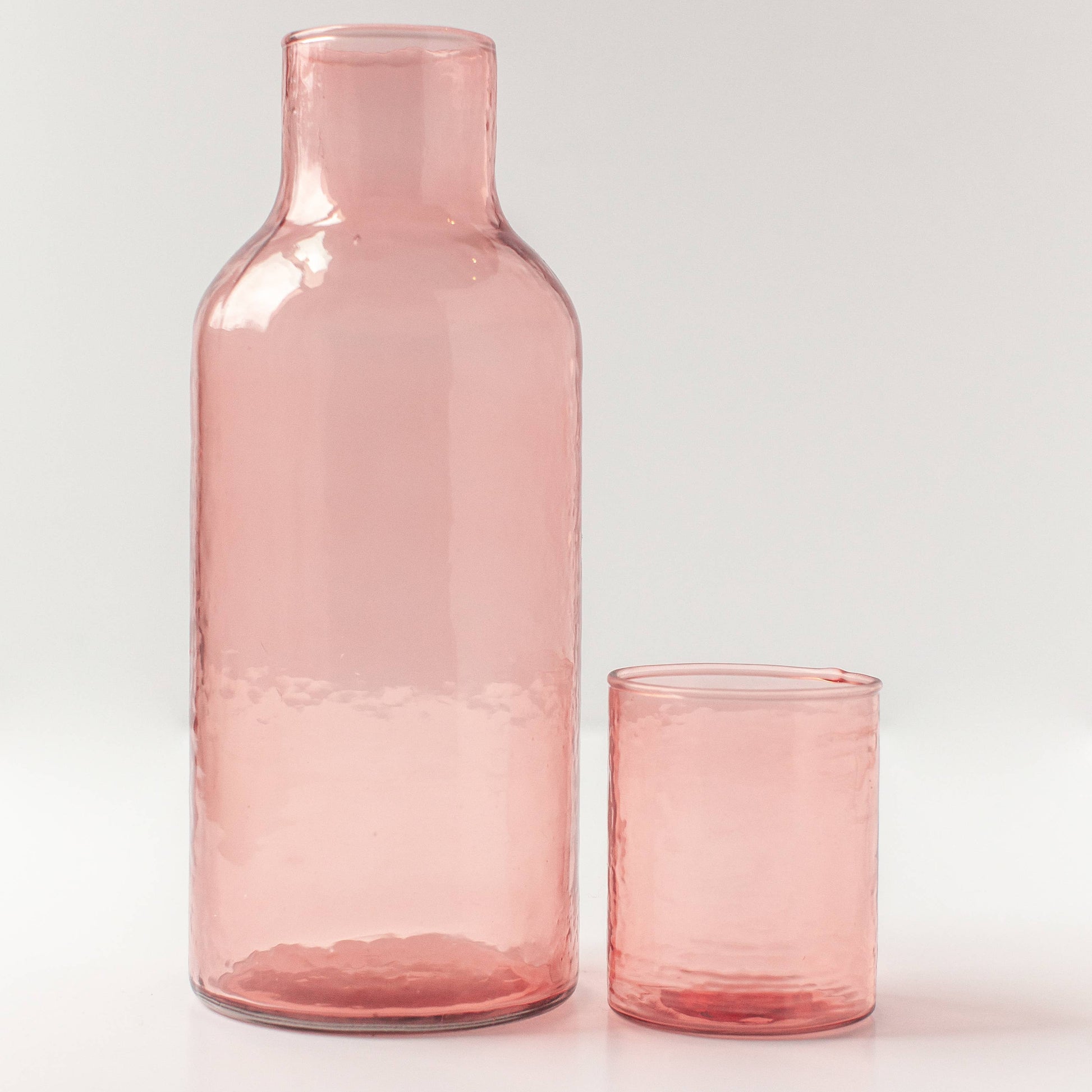Pink glass carafe and tumbler on a light gray background