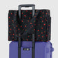 Black patterned bag with red berries on a purple suitcase against a light gray background