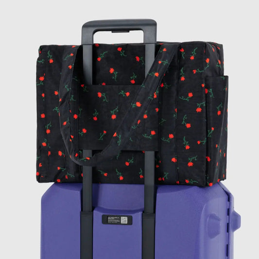 Black patterned bag with red berries on a purple suitcase against a light gray background
