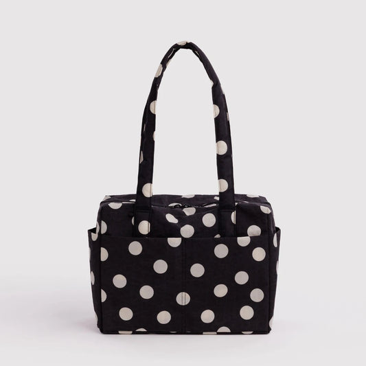A black fabric tote bag with large white polka dots and dual top handles, photographed against a plain light gray studio background.